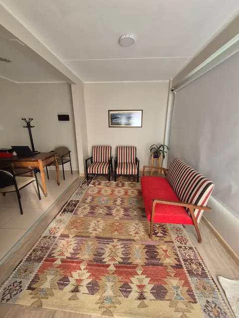 Sala de espera con sillón rojo, butacas a rayas y alfombra tejida
